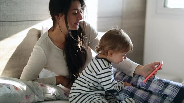 Baby and mother together in bed in the morning holding smartphone device