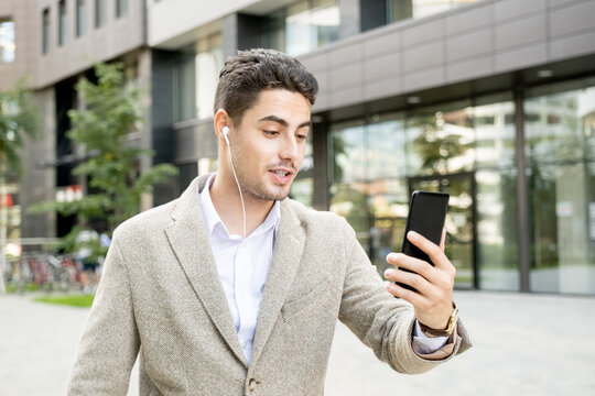 Young mixed-race businessman with earphones looking at smartphone screen