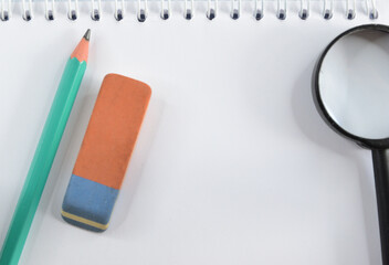 A notebook with a pencil, an eraser and a magnifying glass lying on it