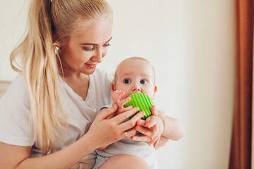 Fototapeta premium Mother playing with her newborn baby son at home. Family having fun. Infant biting ball
