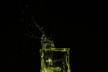 splash of water in a glass by ice cube on black background