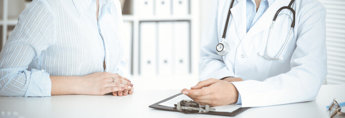 Unknown woman-doctor and patient sitting at the table. Very good news and high level medical service concept