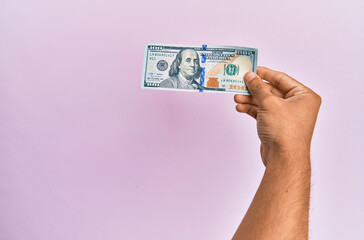 Hispanic hand holding 100 usa dollars banknote over isolated pink background.