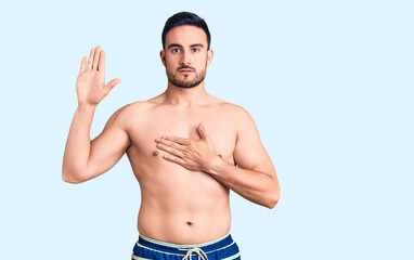 Fototapeta premium Young handsome man wearing swimwear swearing with hand on chest and open palm, making a loyalty promise oath