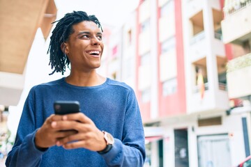 Fototapeta premium Young african american man smiling happy using smartphone at street of city.