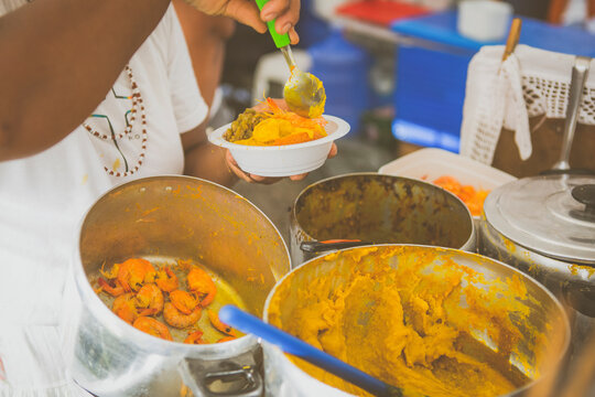 Woman serving vatapa; Brazilian Street food in the streets of Rio de Janeiro, Brazil. Vacation experience exotic food and culture travel destination concept.