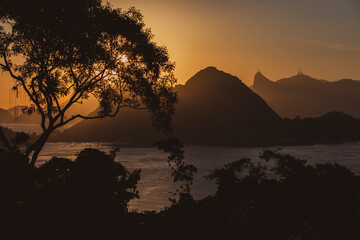 Beautiful view the sea and a chain of mountains silhouette at sunset against orange sky; Mount Corcovado, Rio de Janeiro, Brazil. Trees and vegetation silhouette in the foreground. Copy space for text