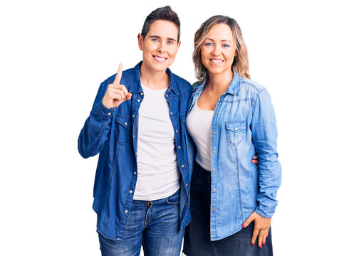 Couple of women wearing casual clothes showing and pointing up with finger number one while smiling confident and happy.