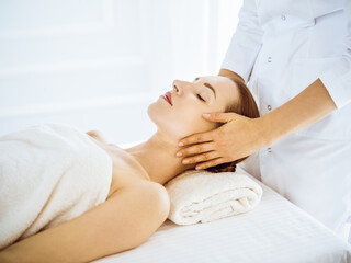 Fototapeta na wymiar Beautiful woman enjoying facial massage with closed eyes in spa center