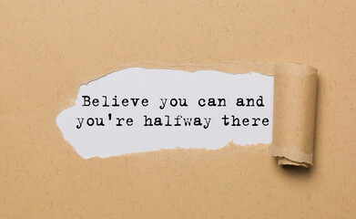 The text Believe you can and you're halfway there, appearing behind torn paper. Motivational quote....