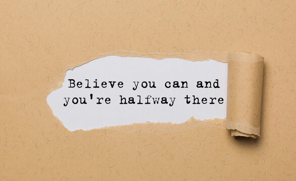 The text Believe you can and you're halfway there, appearing behind torn paper. Motivational quote. The craft paper is ripped.