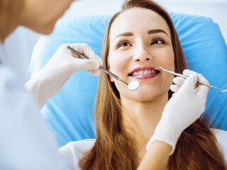 Smiling young woman with orthodontic brackets examined by dentist in dental clinic. Healthy teeth and medical care concept