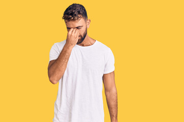 Young hispanic man wearing casual white tshirt tired rubbing nose and eyes feeling fatigue and headache. stress and frustration concept.