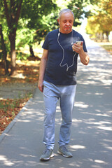 Obraz premium Senior man in sportswear with a smartphone on the street is engaged in fitness. Senior man in sportswear for a walk. The concept of active life in older age.