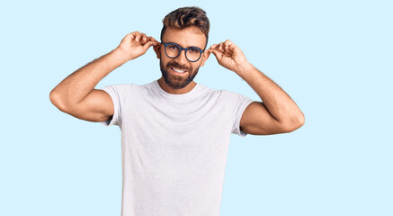 Fototapeta premium Young hispanic man wearing casual clothes and glasses smiling pulling ears with fingers, funny gesture. audition problem