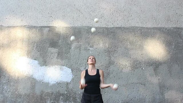A professional juggler juggles with white balls. An attractive female juggler trains her juggling skills. A professional circus actress juggles with white balls on the street.