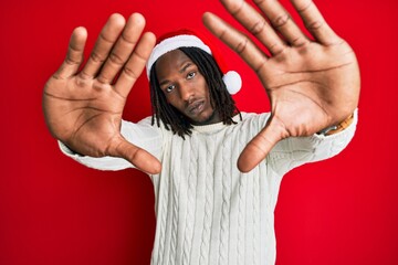 Naklejka premium African american man with braids wearing christmas hat doing frame using hands palms and fingers, camera perspective