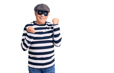Senior handsome man wearing burglar mask and t-shirt celebrating surprised and amazed for success with arms raised and eyes closed. winner concept.
