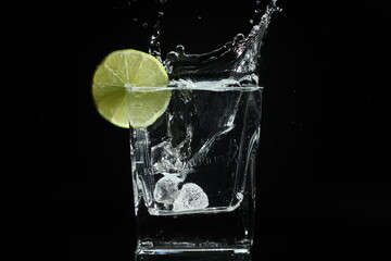splash of water with lime in a glass over ice cube on black background