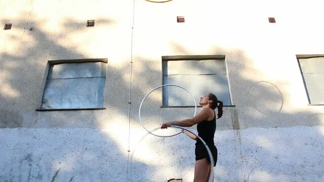 Street Performer Practices Hula Hoop Juggling Skills. Attractive Female, Circus Performer Juggles Hula Hoops On The Street, Improving Her Skills.