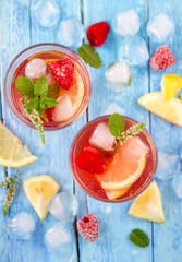 Due bicchieri con un aperitivo, limone, ghiaccio e menta ripresi dall'alto su tavolo dove sono sparse fette di limone, ghiaccio e lamponi 