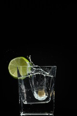 splash of water with lime in a glass over ice cube on black background