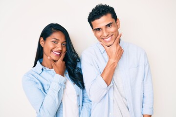 Fototapeta na wymiar Beautiful latin young couple wearing casual clothes looking confident at the camera smiling with crossed arms and hand raised on chin. thinking positive.