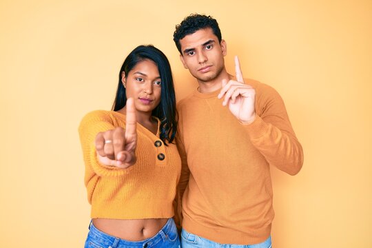 Beautiful latin young couple wearing casual clothes together pointing with finger up and angry expression, showing no gesture