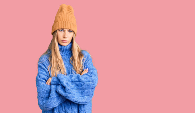 Beautiful caucasian woman with blonde hair wearing wool sweater and winter hat skeptic and nervous, disapproving expression on face with crossed arms. negative person.