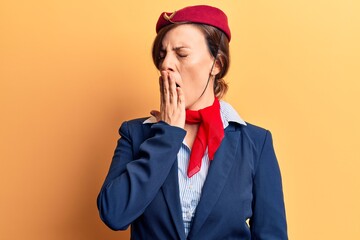 Young beautiful woman wearing stewardess uniform bored yawning tired covering mouth with hand. restless and sleepiness.