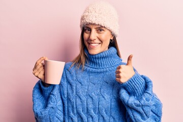 Young beautiful woman wearing winter clothes holding coffee smiling happy and positive, thumb up doing excellent and approval sign