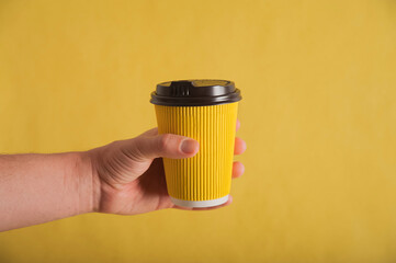 Hand with yellow nails holds a paper cup on a yellow background close-up and copy space. Monochrome yellow.