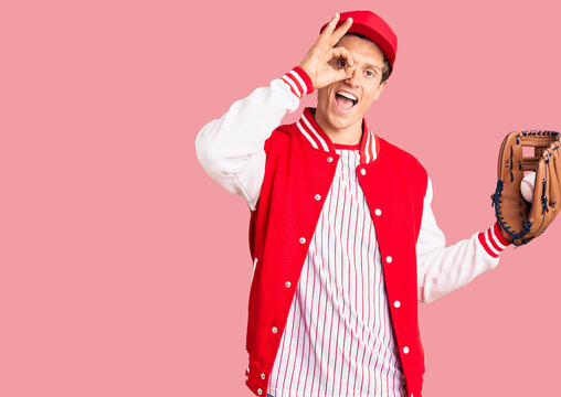 Young handsome man wearing baseball uniform holding golve and ball smiling happy doing ok sign with hand on eye looking through fingers