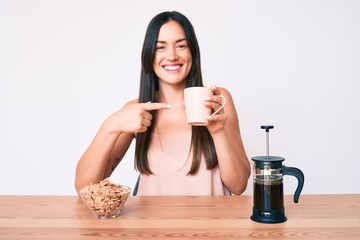 Young caucasian woman sitting at the table drinking coffee smiling happy pointing with hand and finger