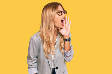 Beautiful blonde young woman wearing business clothes shouting and screaming loud to side with hand on mouth. communication concept.