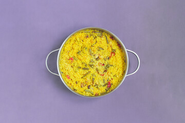 Typical Spanish dish made with rice, vegetables, and seafood in a huge saucepan with handles on a textured purple tablecloth and space to input a text. Cooking healthy vegetarian food at home.