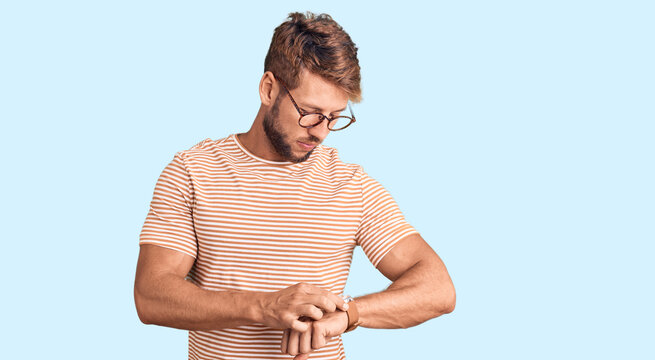 Young caucasian man wearing casual clothes and glasses checking the time on wrist watch, relaxed and confident