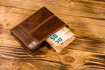 Brown leather wallet with fifty euro banknotes on the wooden background