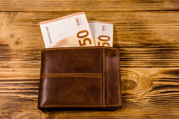 Brown leather wallet with fifty euro banknotes on the wooden background. Top view