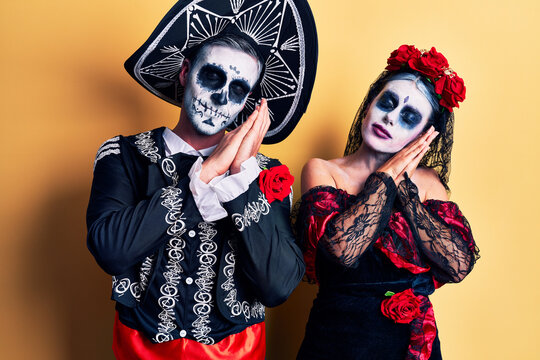 Young couple wearing mexican day of the dead costume over yellow sleeping tired dreaming and posing with hands together while smiling with closed eyes.