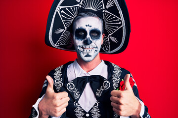 Young man wearing mexican day of the dead costume over red success sign doing positive gesture with hand, thumbs up smiling and happy. cheerful expression and winner gesture.