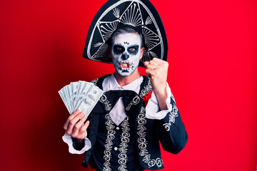 Young man wearing mexican day of the dead costume holding dollars annoyed and frustrated shouting with anger, yelling crazy with anger and hand raised