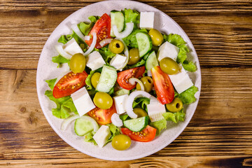 Ceramic plate with greek salad on wooden table. Top view