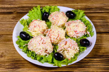 White plate with crab-cheese balls and lettuce leaves on wooden table