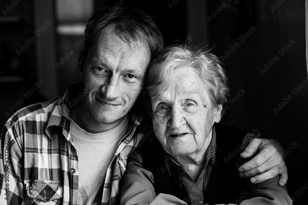 Poster Portrait of man embracing his old grandmother. Black and white photo.