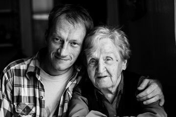 Portrait of man embracing his old grandmother. Black and white photo.