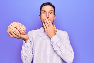 Young handsome man asking for care memory holding brain over isolated purple background covering...