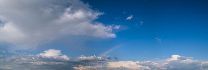 Naklejka na ściany i meble White cumulus clouds and rainbow in blue sky panoramic high resolution background