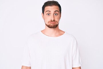 Young handsome man wearing casual white tshirt puffing cheeks with funny face. mouth inflated with air, crazy expression.