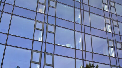 Blue curtain wall made of toned glass and steel constructions under blue sky. A fragment of a building.